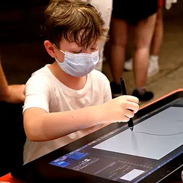 Rimini Comix, stand della scuola, un bambino che disegna con attrezzatura professionale Wacom messa a disposizione dalla scuola – Rimini 2021